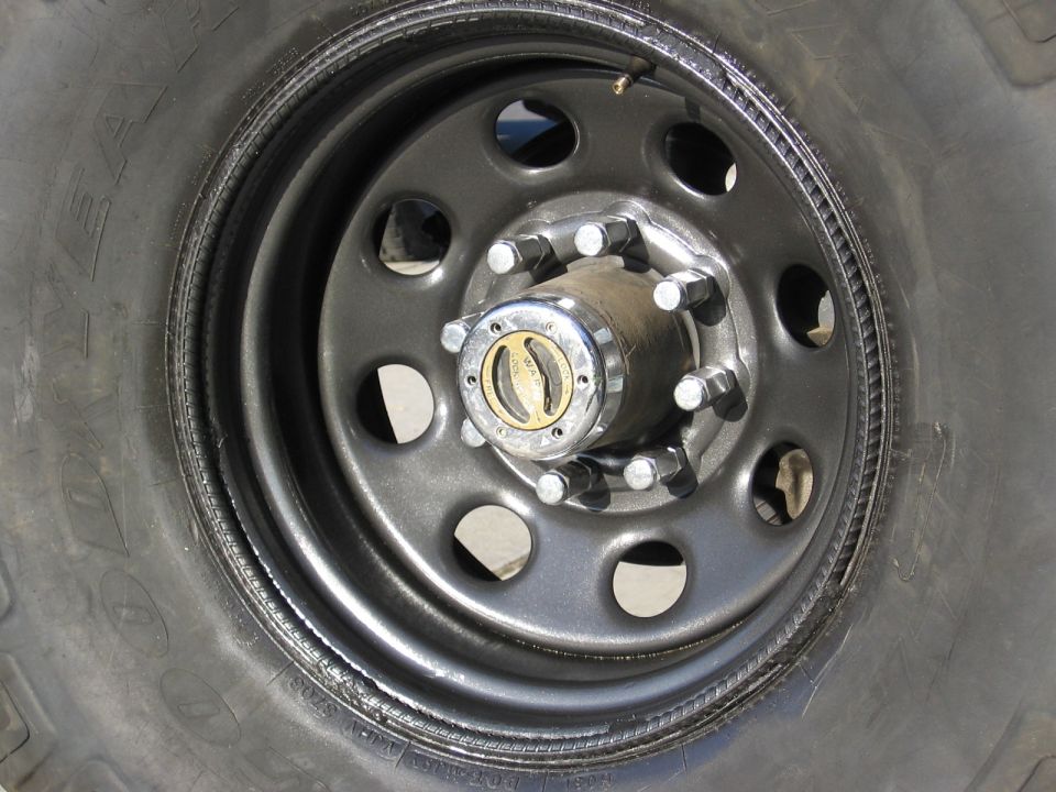 Black eight-lug steel wheel on Goodyear mud tire with chrome Warn manual locking hub