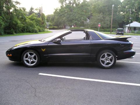 1984 Pontiac Fiero - This black convertible sports car features a distinctive yellow stripe and a rear spoiler, seen from the side.