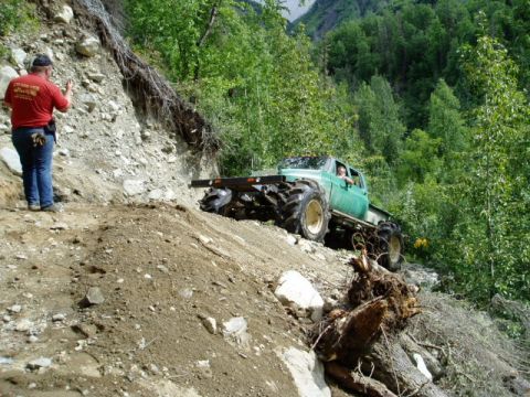 2000 Ford E350 - A heavily modified truck navigates a challenging off-road incline with a person observing from the side.