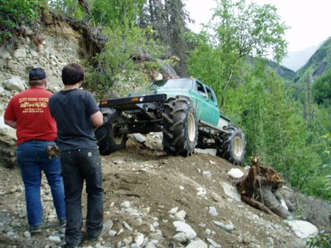 2000 Ford E350 - A heavily modified truck navigates a steep, rocky incline in a wooded area.