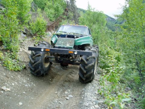 2000 Ford E350 - This heavily modified truck navigates a rough, wooded terrain with its oversized agricultural tires.