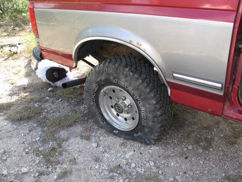 1995 Ford Bronco - Flat tire on a red and silver pickup truck requires attention.