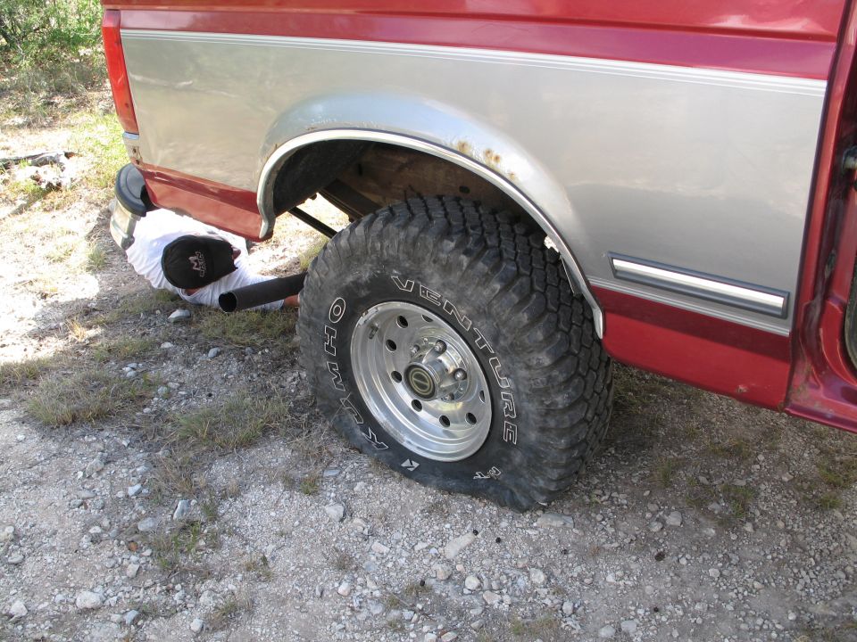 Person under a red and silver pickup truck with a flat tire