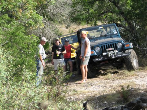 1995 Ford Bronco - Two Jeeps are parked on a dirt trail surrounded by trees, with four people standing around them.