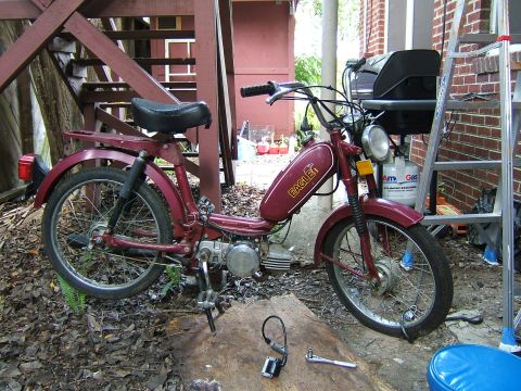 1996 Ford Probe - A maroon moped with an 'Eagle' logo on the gas tank is parked on a wooden surface outdoors, with a ladder and grill in the background.