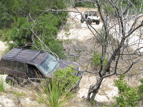 1995 Ford Bronco - A dark SUV is stuck in the brush off a dirt road, with another vehicle visible in the distance.