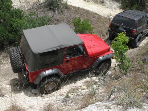 1995 Ford Bronco - Two off-road vehicles navigate a challenging rocky trail under daylight conditions.