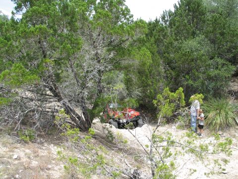 1995 Ford Bronco - A red ATV is partially hidden by trees, with two people observing it in a wooded area.