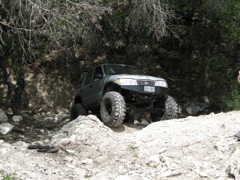1995 Ford Bronco - A modified silver SUV with large off-road tires tackles a challenging rocky terrain.