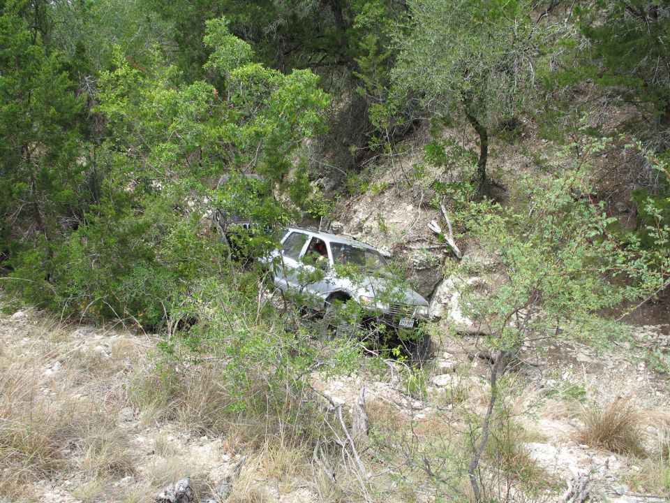 Silver 1995 Ford Bronco partially obscured by trees, tilted on a rocky incline