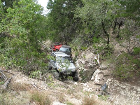 1995 Ford Bronco - Several off-road vehicles navigate a challenging, wooded trail.