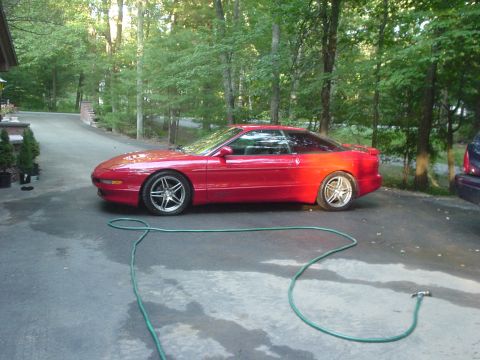 1995 Ford Probe - A red 1995 Ford Probe is parked on a wet driveway surrounded by trees.