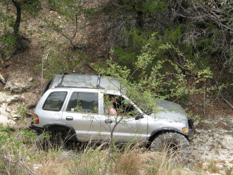 1995 Ford Bronco - SUV navigating difficult terrain in a wooded, rocky environment.
