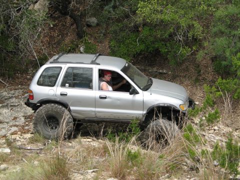 1995 Ford Bronco - A silver Kia Sportage navigates a , wooded terrain with large, aggressive tires.