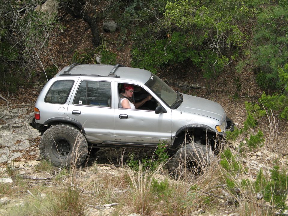 Silver Kia Sportage with large off-road tires driving on a rocky trail