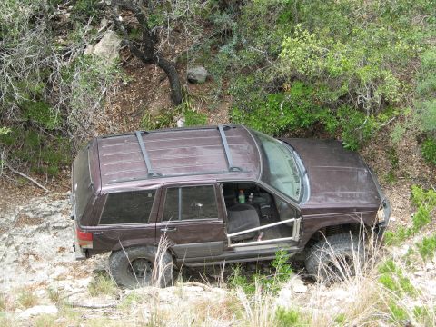 1995 Ford Bronco - A brown Jeep Grand Cherokee is parked on a rocky, wooded hillside with its driver's door open.