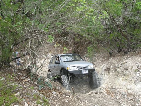 1995 Ford Bronco - Silver SUV tackling a challenging off-road trail with significant elevation change.