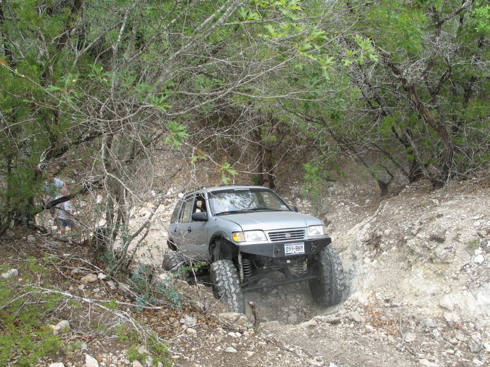 Silver SUV with aftermarket bumper and large tires navigating a steep, rocky incline