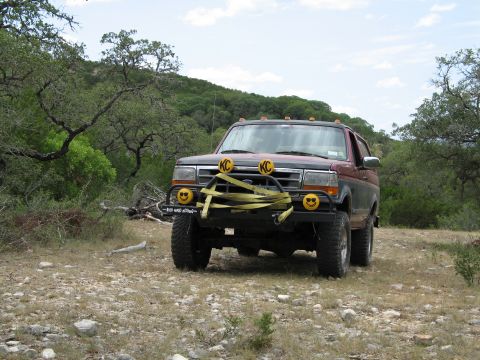 1995 Ford Bronco - A maroon and black Ford Bronco is parked on a rocky, dirt path in a wooded area.