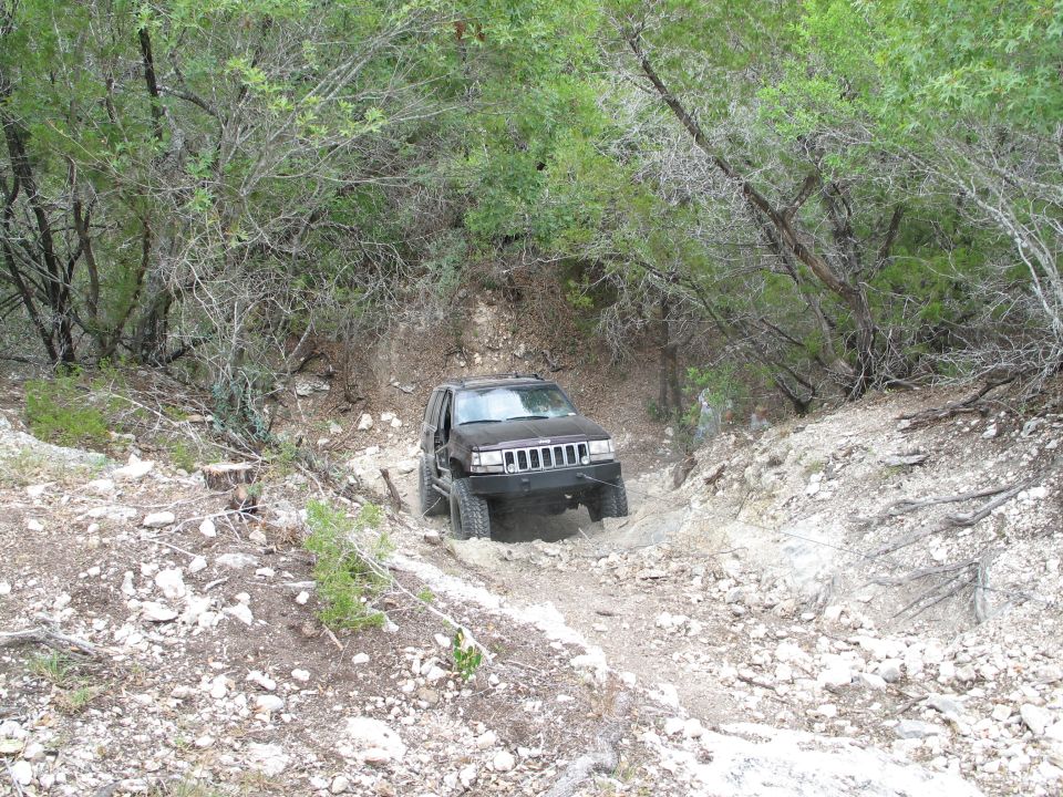 Dark Jeep Grand Cherokee driving on a rocky, wooded trail