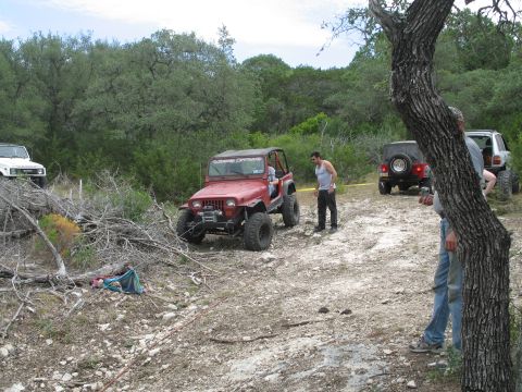 1995 Ford Bronco - Several off-road vehicles, including a red Jeep Wrangler, navigate a rocky, wooded trail during an outing.