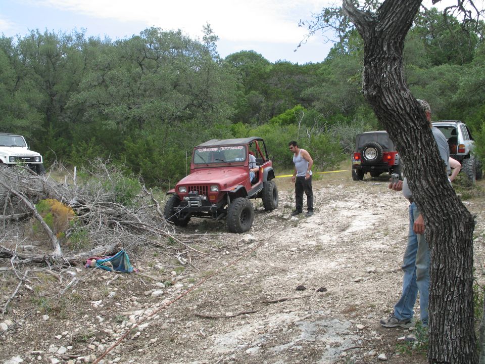 Red Jeep Wrangler with winch on rocky trail, other off-road vehicles visible