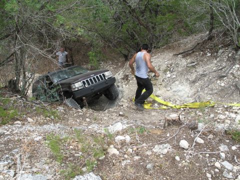 1995 Ford Bronco - A Jeep Grand Cherokee is stuck on a steep, rocky trail with a person attempting to pull it out with a tow strap.