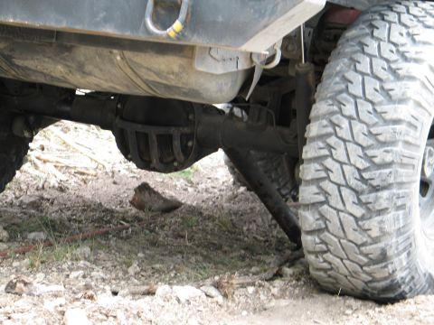 1995 Ford Bronco - Close-up view of the rear axle and a large off-road tire on a vehicle parked on rough terrain.