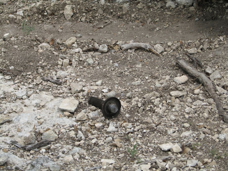 Driveshaft U-joint part lying on rocky ground with scattered debris and branches