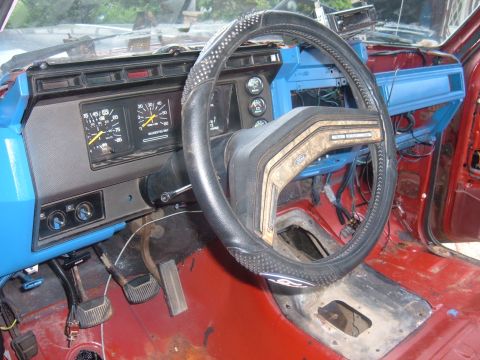 1985 Ford F-150 - Interior of a red truck with blue dashboard accents and a steering wheel. The dashboard is missing some components.
