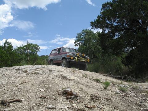 1995 Ford Bronco - This Ford Bronco is navigating a rough, off-road terrain under a partly cloudy sky.