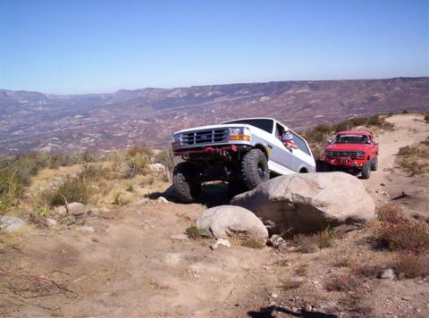 1995 Ford Bronco - Two Ford trucks, a Bronco and a pickup, navigate a challenging rocky terrain on a sunny day.
