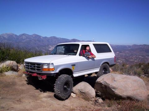 1995 Ford Bronco - A man drives a white Ford Bronco on a rocky mountain trail under a clear blue sky.
