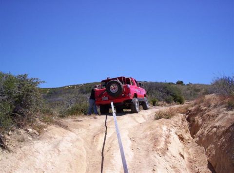 1995 Ford Bronco - A red SUV is being pulled up a steep, rutted dirt path by a strap under a clear blue sky.