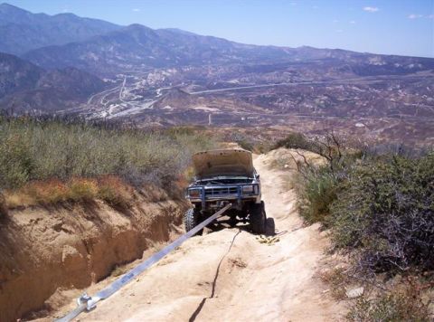 1995 Ford Bronco - A blue Ford Bronco is stuck on a steep dirt trail, with its hood open and a tow strap attached.