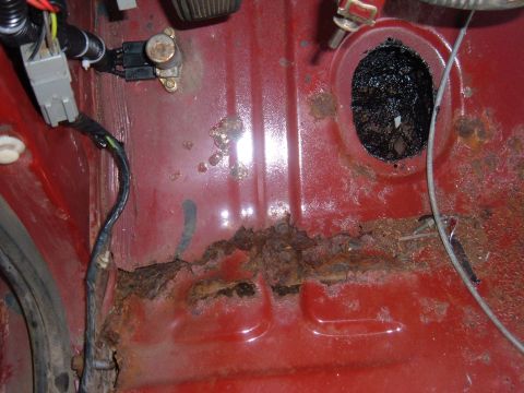 1985 Ford F-150 - Extensive rust has compromised the floor pan of this 1985 Ford F-150, with wiring visible near the corroded areas.