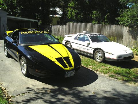 1984 Pontiac Fiero - Two Pontiacs are parked in a driveway. The white car is labeled 'Official Race Car'.