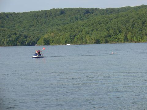 1988 Ford Bronco - Two people ride a jet ski on a calm lake, with a wooded hillside in the distance.
