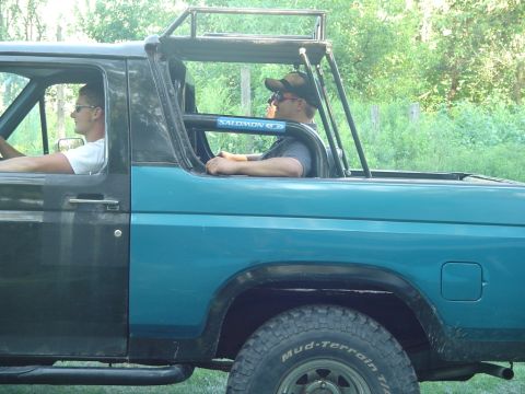1986 Ford Bronco - This 1986 Ford Bronco features a custom top with a prominent roll cage and roof rack, seen from the side.