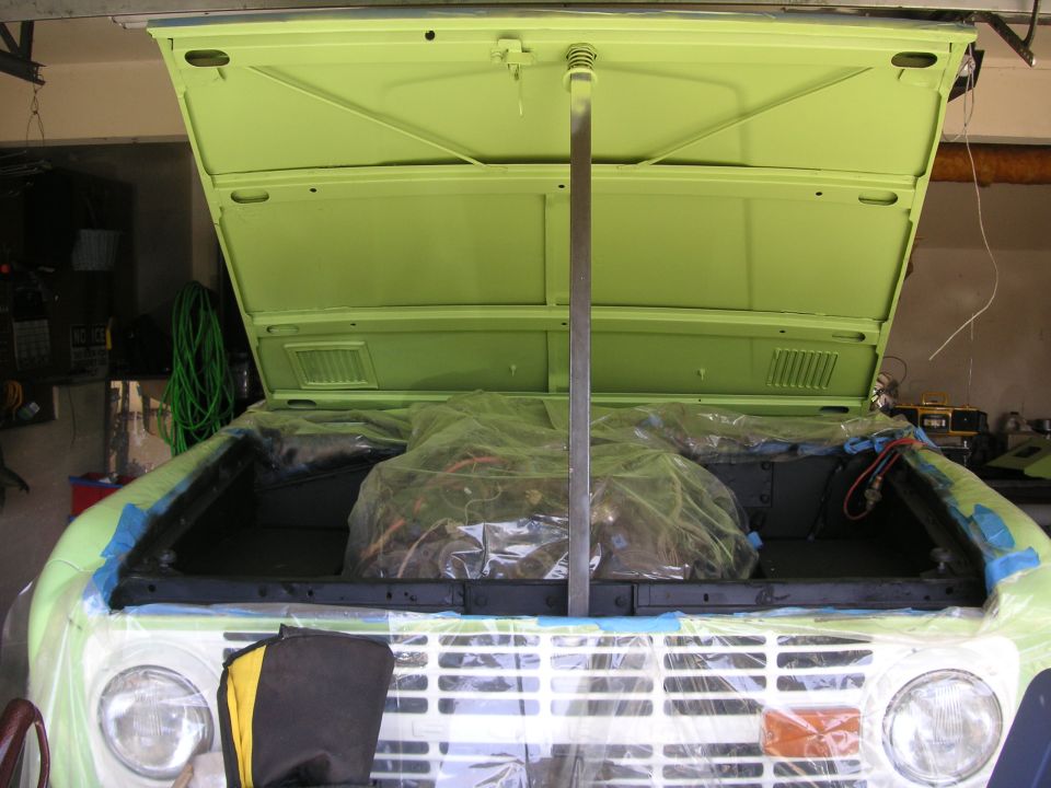 Green classic SUV with hood open, engine covered in plastic wrap