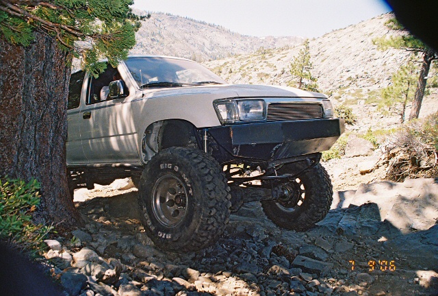 White pickup truck with aftermarket bumper and large tires on a rocky trail