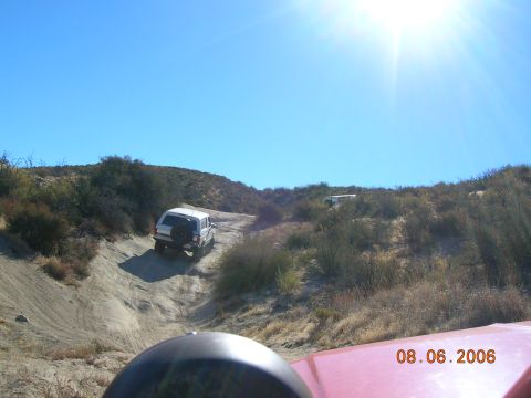 1985 Ford Bronco - Multiple SUVs navigate a dusty off-road trail under a bright sun.