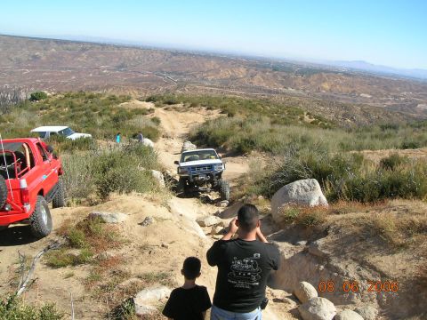 1985 Ford Bronco - Multiple off-road vehicles navigate a challenging dirt path in a scenic, arid landscape.