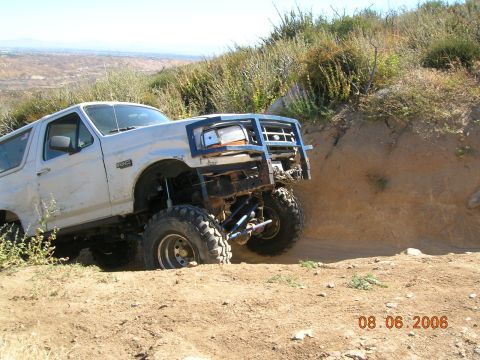 1985 Ford Bronco - This modified Ford Bronco is stuck on a steep dirt incline, showing its off-road capabilities.