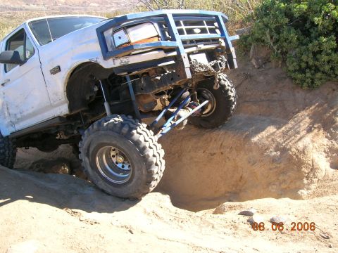 1985 Ford Bronco - A modified Ford truck navigates a steep dirt incline on an off-road trail.