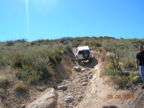 1985 Ford Bronco - Off-road vehicle tackles a challenging rocky trail under a clear blue sky.