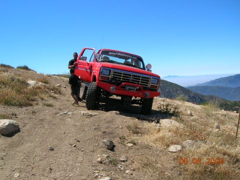 1985 Ford Bronco - A red Ford truck is parked on a dirt path on a mountainside with a scenic view of the valley below.