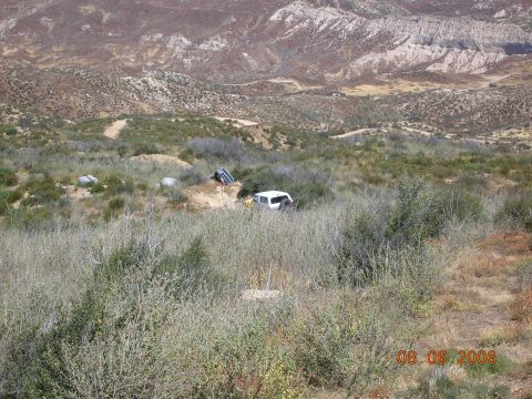 1985 Ford Bronco - A white SUV is parked on a dirt embankment surrounded by dry vegetation and hills in the background.