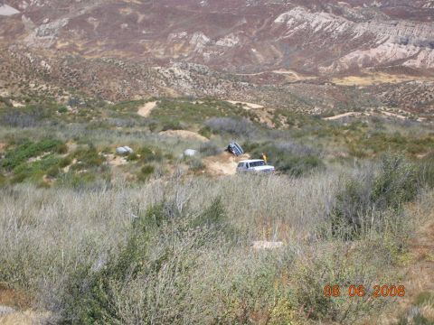 1985 Ford Bronco - A white SUV is seen off-roading on a dirt path in a , arid environment with another vehicle partially visible.