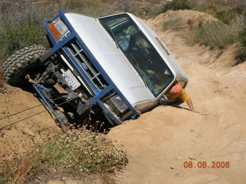 1985 Ford Bronco - Off-road Bronco stuck in dirt with driver attempting to get out.